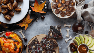 various treats including chocolate bark, stuffed dates, apples and caramel, and gummy pieces on plates on a gray background