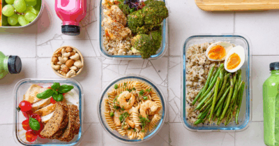 a cracked stone background with glass containers filled with grains, veggies, a soft boiled egg and 3 bottles of juice