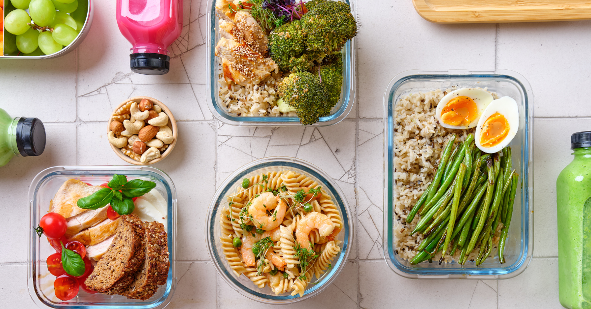 a cracked stone background with glass containers filled with grains, veggies, a soft boiled egg and 3 bottles of juice